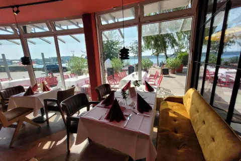 Gemütliche Tische mit rotem Stoff und Blick aufs Wasser – hier könnte das beste Restaurant in Waren sein.