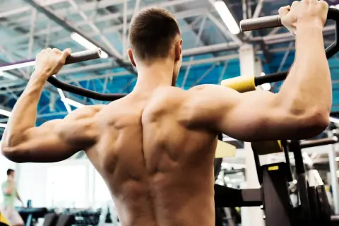 Un homme musclé effectue un tirage vertical, ses muscles dorsaux bien dessinés sous l'effort.