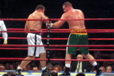 Two boxers in a ring, one in white shorts, the other in green. This bout adheres to the light heavyweight boxing weight limit.