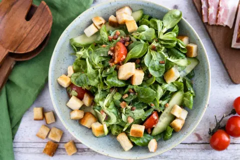 Frischer Feldsalat mit Speck und knusprigen Croutons, garniert mit Tomaten und Gurkenscheiben. Ein Genuss!
