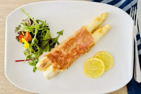 Spargel Cordon Bleu, knusprig paniert, serviert mit frischem Salat und Zitronenscheiben auf einem weißen Teller.