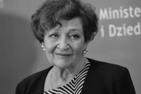 Uśmiechnięta Ewa Dałkowska, z perłami w uszach, na tle napisu "Ministerstwo i Dziedzictwo".
