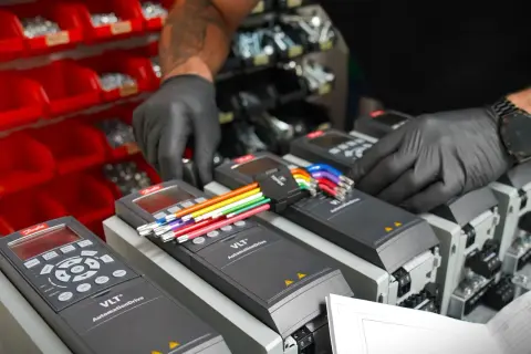 Ręce w czarnych rękawiczkach podłączają kolorowe przewody do falowników VLT AutomationDrive, kluczowych dla sterowania wektorowego.