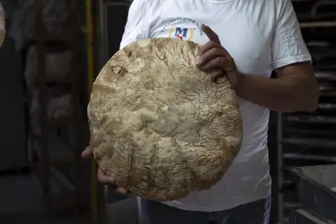 Un fornaio mostra un grande pane rustico, la cui crosta ricorda la ricetta del pane di Monte Sant'Angelo.