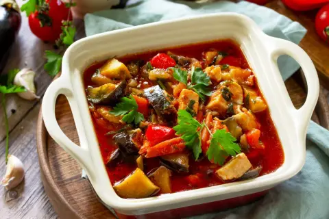 Pyszny gulasz z kurczaka z bakłażanem i papryką, udekorowany natką pietruszki. Aromatyczne danie w białej zapiekance.