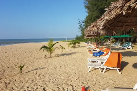 Solig strand på Koh Kho Khao med solstolar, parasoller och en volleybollplan.