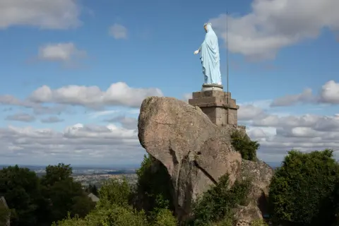Statue de la Vierge sur la butte de Suin, veillant sur la vallée sous un ciel bleu parsemé de nuages.