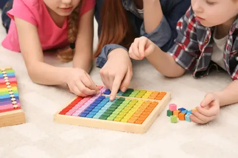 Kinder lernen spielerisch Mathematik im Kindergarten mit bunten Holzbausteinen und einer Multiplikationstafel.