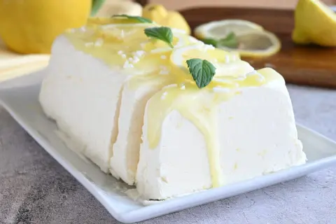 Un delizioso semifreddo al limone, guarnito con scorzette, menta e una glassa gialla, pronto per essere gustato.