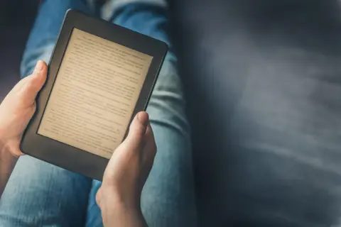 Personne lisant un livre sur une tablette ou liseuse, confortablement installée dans son jean.