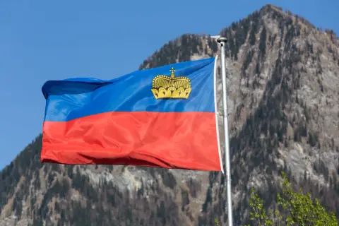 Flaga Liechtensteinu powiewa na tle gór. Wartość tej waluty, franka szwajcarskiego, jest stabilna.
