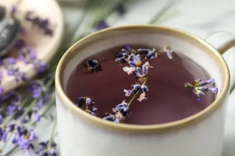 Aromaticzna herbata lawendowa w kubku, z kwiatami lawendy unoszącymi się na powierzchni. W tle widać gałązki lawendy.