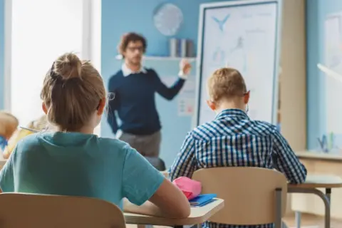 Nauczyciel tłumaczy lekcję, a uczniowie siedzą w ławkach. Czy wysokie zarobki nauczycieli wpłyną na jakość edukacji?