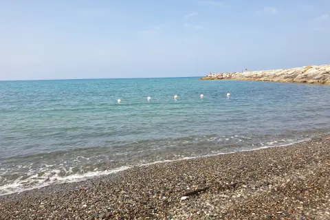 Spiagge più belle della Marina di Cecina: mare azzurro, ciottoli levigati e un molo roccioso con qualche bagnante.