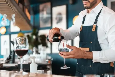 Doświadczony sommelier wina nalewa czerwone wino do kieliszka w eleganckiej restauracji.