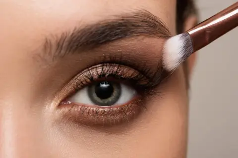Occhio con trucco elegante, sfumature bronze e un pennello che applica l'ombretto.