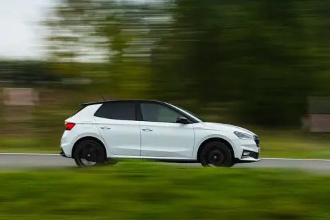 Un Skoda Fabia 130 blanco con techo negro se mueve rápido por una carretera rural, con el paisaje difuminado por la velocidad.