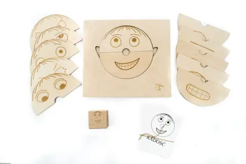 Drewniane pomoce dydaktyczne do nauki emocji: puzzle twarzy, kostka i karty z buźkami.