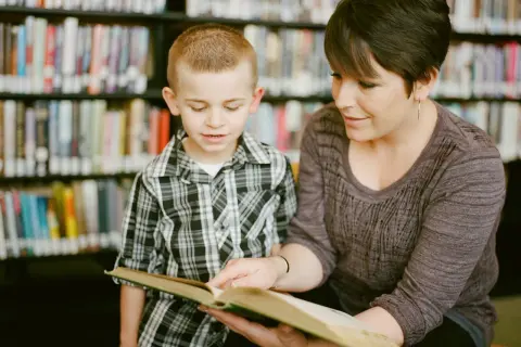 Kobieta i chłopiec czytają książkę w bibliotece. Pokazuje to, jak czytanie książek wpływa na człowieka, rozwijając wyobraźnię i wiedzę.