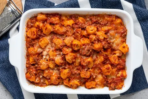 Tortelli ripieni di carne al forno, ricoperti di sugo rosso e formaggio fuso, pronti per essere gustati.