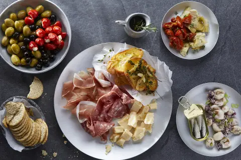 Plateau de charcuterie, fromages, olives, tomates séchées, artichauts, toasts à l'ail et sardines. Une recette antipasti italien facile pour un apéritif gourmand.