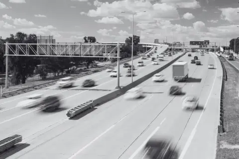 Rozmyte samochody pędzą po wielopasmowej autostradzie. Widoczny znak drogowy i wiadukt. Specustawa drogowa w akcji.