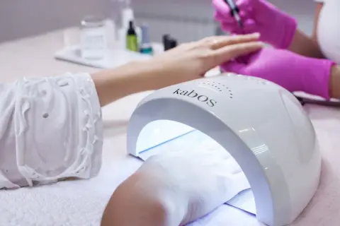 Dłoń w lampie UV do paznokci. Zastanawiasz się, ile trzymać bazę w lampie? Czas utwardzania zależy od produktu.