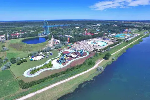 Mirabilandia, un parco acquatico con scivoli colorati e piscine, si trova vicino a un lago, con una ruota panoramica sullo sfondo.