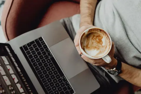 Osoba z kawą na laptopie, ucząca się Mac OS dla początkujących.