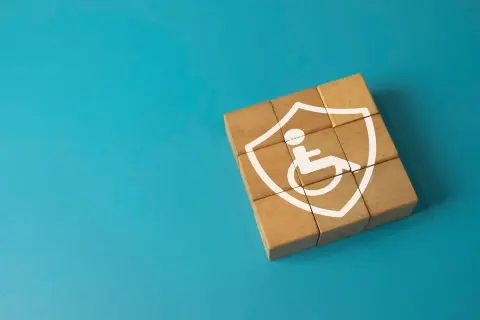 Drewniane klocki tworzą tarczę z symbolem osoby na wózku, symbolizującą wsparcie i ochronę dla osób z niepełnosprawnością intelektualną.