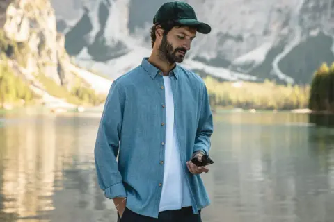 Un homme porte une chemise bleue décontractée, dont la matière légère est parfaite pour une journée au bord du lac.