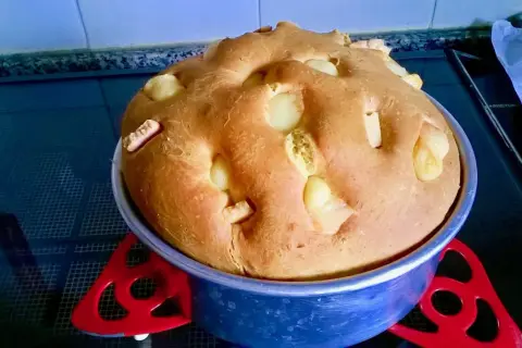 A golden-brown, round bread with chunks of white cheese baked into the top, in a blue baking pan.