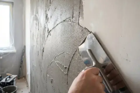 Ręka z kielnią rozprowadza gładką masę gipsową na ścianie, przygotowując ją do malowania.