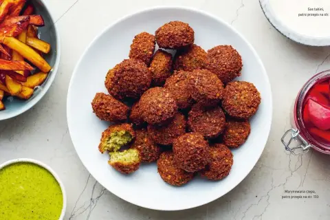 Talerz pełen chrupiących kulek falafela, które są smażonymi kotlecikami z ciecierzycy. Obok frytki i sosy.