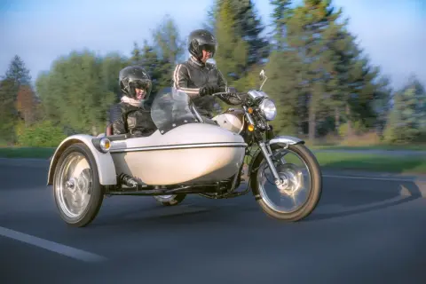 Para podróżuje motocyklem z koszem, ciesząc się jazdą po malowniczej drodze.