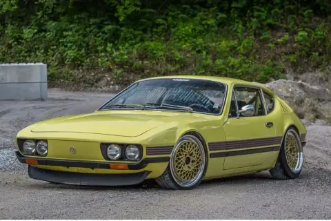 Gul vw sp2 med guldfärgade fälgar står på grusväg.