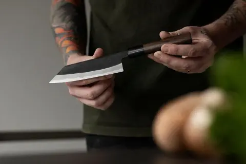 Manos sostienen un cuchillo de chef con hoja de acero VG10, listo para cortar.