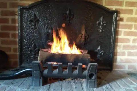 Un feu crépite dans une cheminée en briques, avec un système discret pour récupérer la chaleur d'un conduit de cheminée.