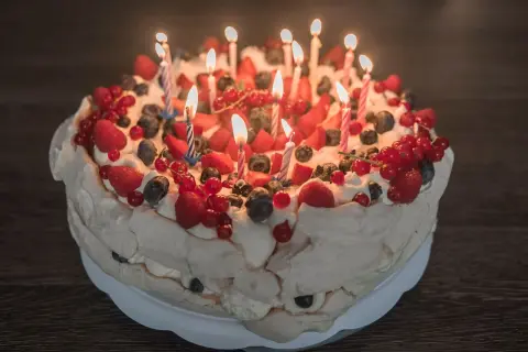 Pyszne ciasto urodzinowe Pavlova ozdobione bitą śmietaną i świeżymi owocami, z płonącymi świeczkami.