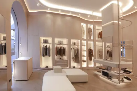 Interni negozio di abbigliamento con abiti eleganti appesi, borse e scarpe in esposizione. L'ambiente è moderno e luminoso, con un design minimalista e finiture in legno chiaro.