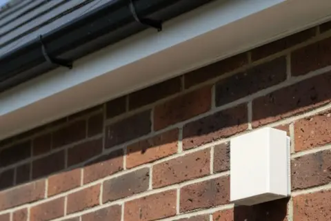 Boîtier blanc fixé sur un mur de briques, sous une gouttière. Peut-être lié à un problème sonde extérieure chaudière.