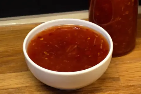 En skål med söt chili sås, med en flaska i bakgrunden. Perfekt för dippning eller som smakförhöjare.
