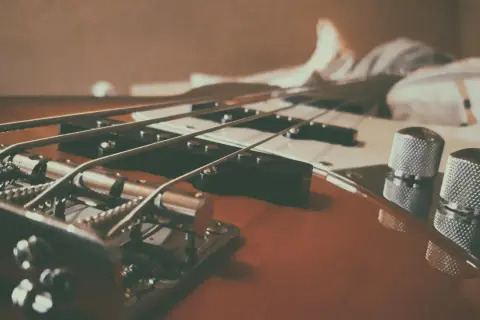 Nahaufnahme eines E-Basses, der sich vom E-Gitarre durch dickere Saiten und einen tieferen Klang unterscheidet.