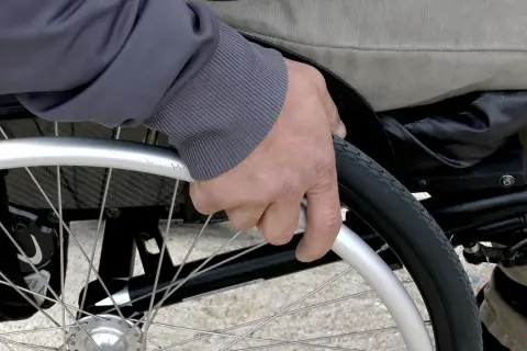 Mano che afferra la ruota di una sedia a rotelle per anziani, un ausilio essenziale fornito dall'ASL per garantire mobilità e autonomia.