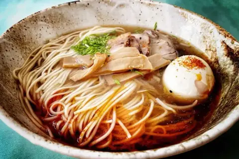 A miseczce shoyu ramen z makaronem, plastrami mięsa, bambusem i jajkiem na twardo, posypane przyprawami.