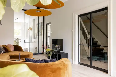 Luxe vestibule woning met oranje bank, glazen deuren naar de trap en een tv-hoek.