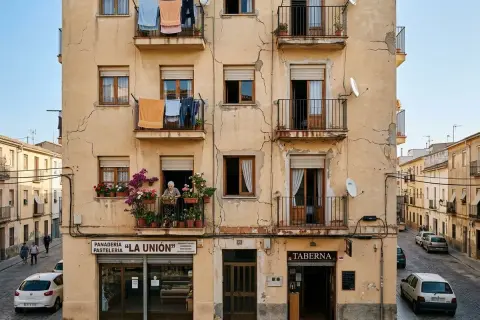 Edificio con fachada exterior agrietada, ropa tendida en balcones y una anciana cuidando flores. Necesita reparar fachada exterior.