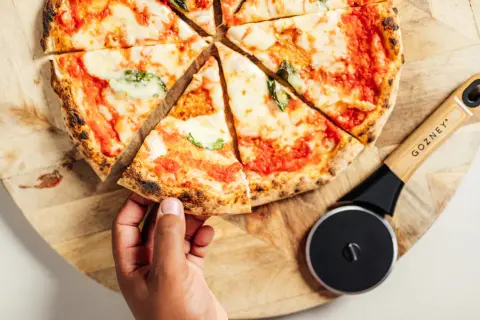 Une main prend une part de pizza maison, fraîchement coupée, prête à être dégustée. Idéal pour congeler pizza maison et en profiter plus tard.