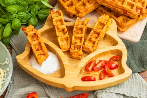 Leckere Pizza-Waffeln mit Mais und Paprika, serviert auf einem Kinder-Teller mit Tomaten und Dip. Ein Hit für kleine Feinschmecker!