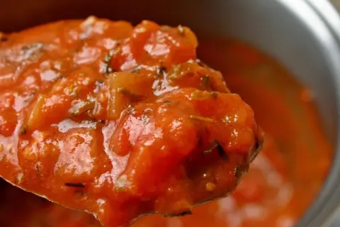 Cuchara llena de passata de tomate casera, con trozos de tomate y hierbas aromáticas.
